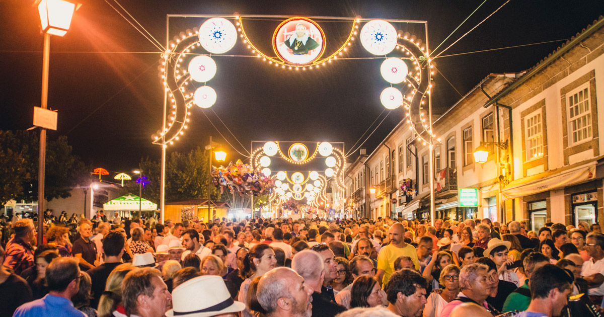 Rua principal de Ponte da Barca cheia de gente à noite, sob os arcos de iluminação da Romaria de São Bartolomeu